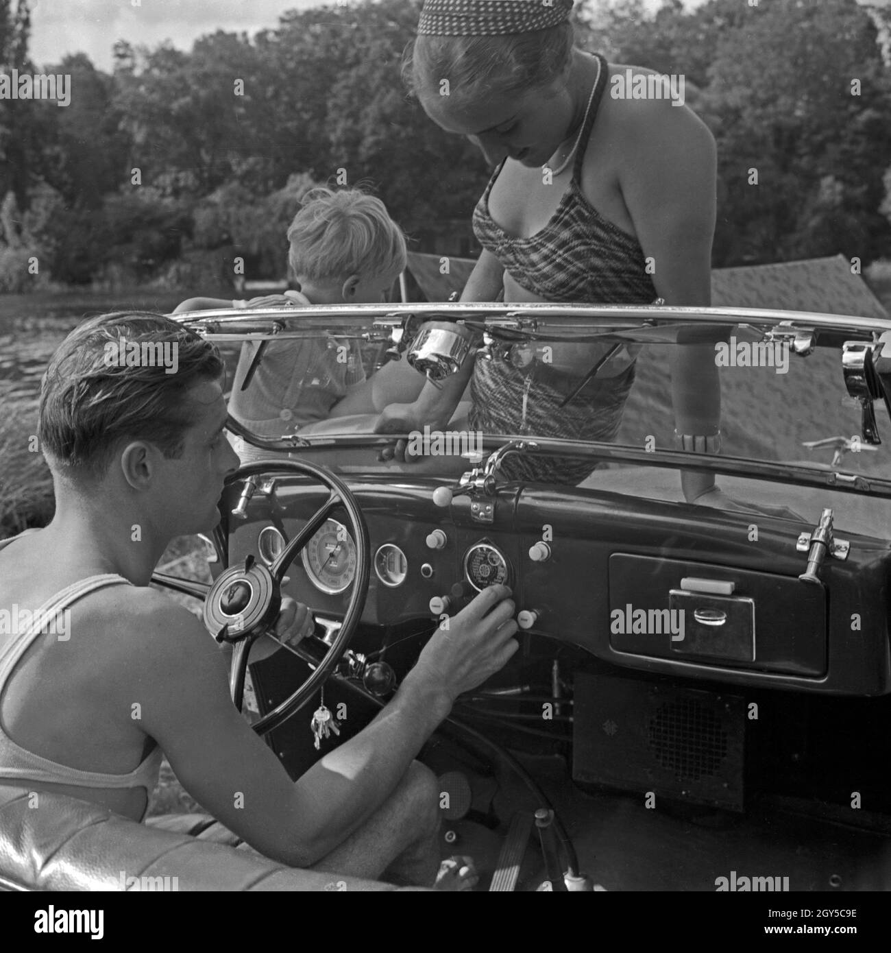 Ein Mann am Steuer eines Ford V8 Cabrio, eine junge Frau und ein kleiner Junge schauen über die Windschuutzscheibe zu, Deutschland 1930 er Jahre. Un homme au volant de sa Ford V8 décapotable, une jeune femme et un petit garçon le regarder jouer avec les voitures, Allemagne 1930. Banque D'Images