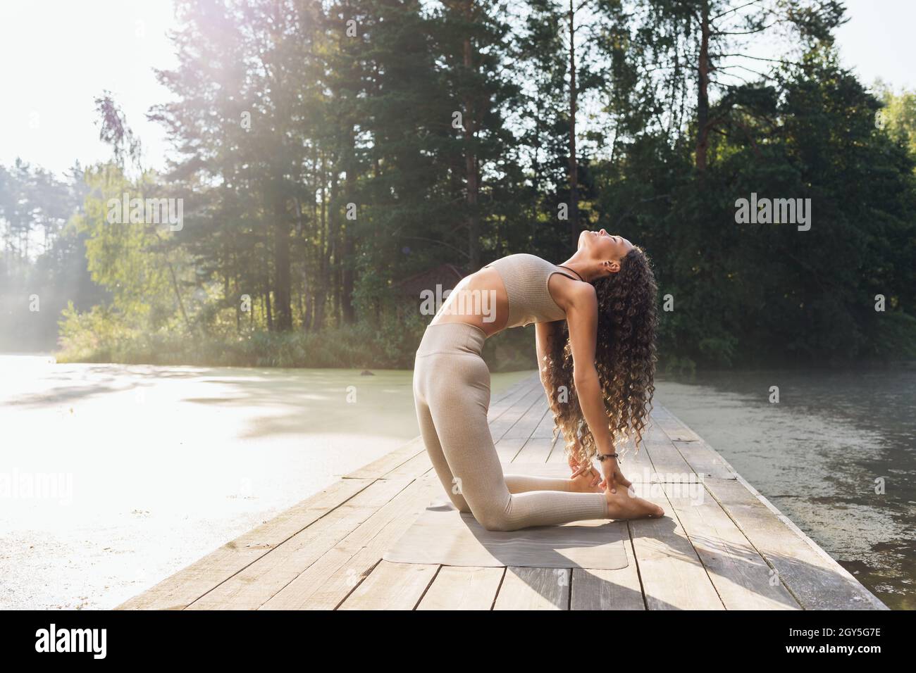 Une femme en sport pratiquant le yoga exécute l'exercice Ushtrasana, pose de chameau, s'exerçant à l'extérieur dans un parc près de l'étang Banque D'Images
