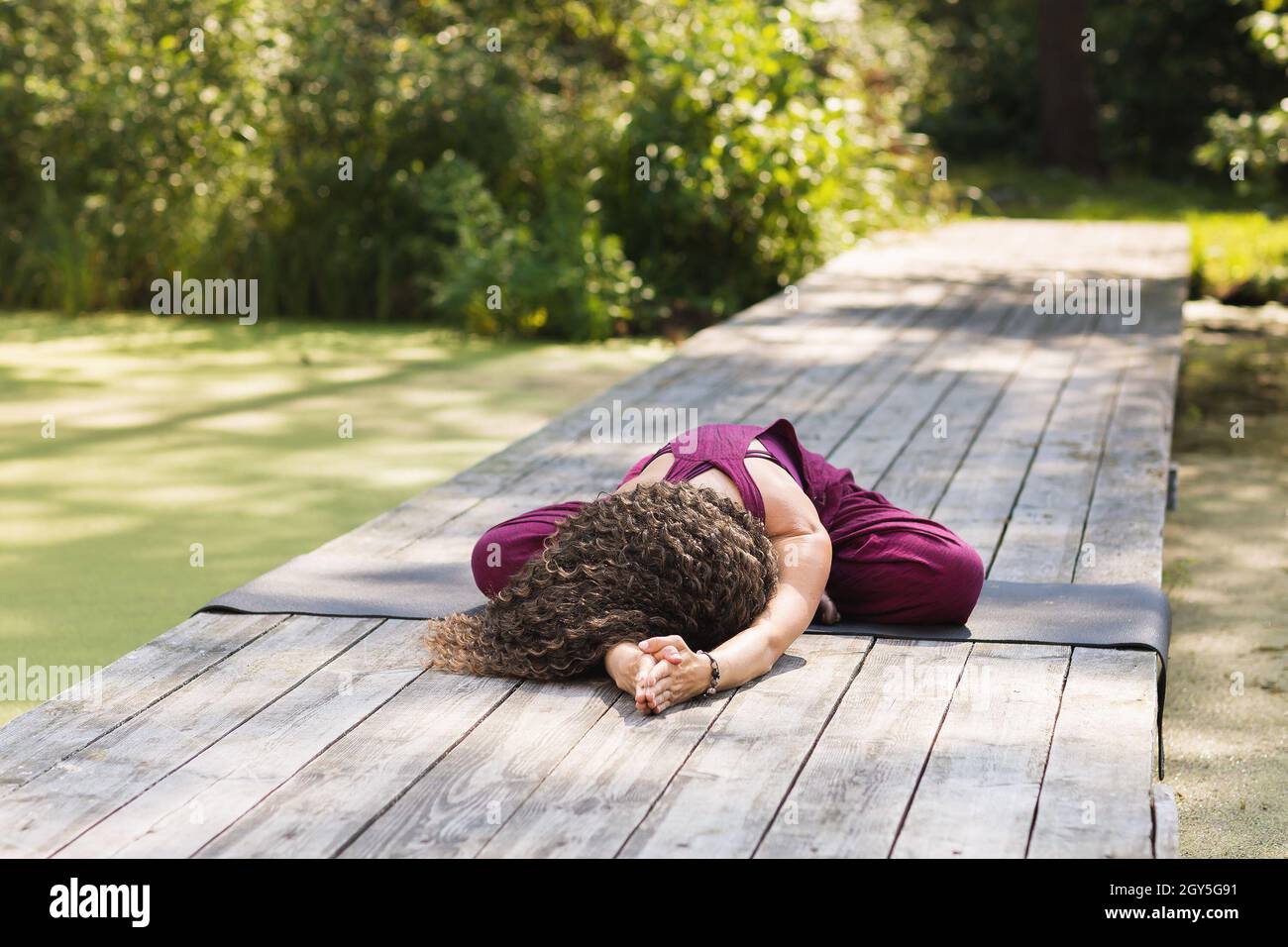 Femme effectuant un exercice de balasana assis sur un tapis dans le parc un matin ensoleillé, pose d'enfant Banque D'Images
