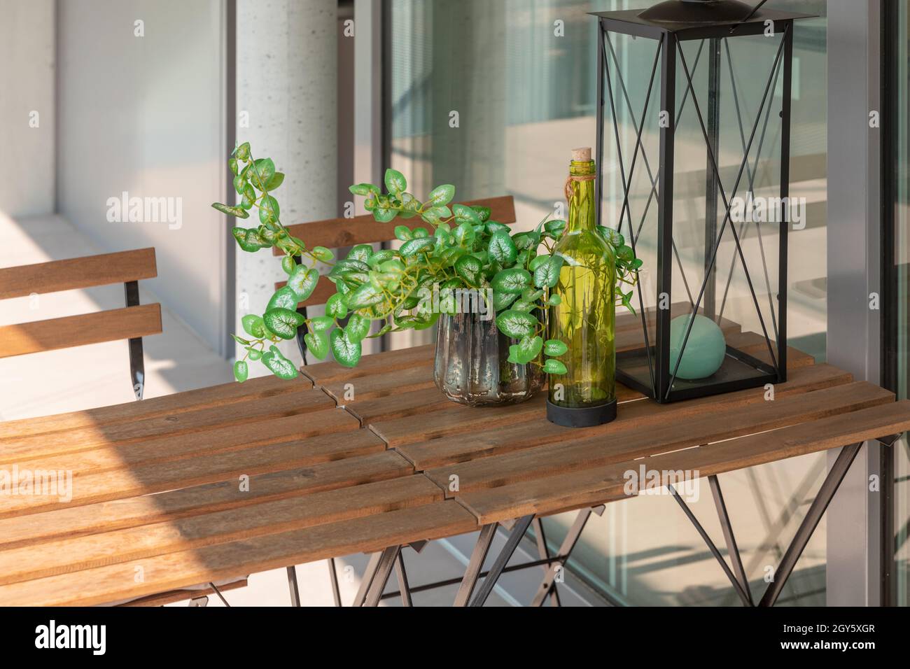 Terrasse moderne avec table et chaises en bois.Une plantule, une bouteille et une lanterne sur la table.Journée ensoleillée en été. Banque D'Images