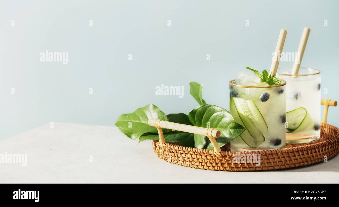 Eau vitaminée d'été tendance et saine avec concombre, menthe et myrtille dans plateau en osier sur fond bleu ciel, bannière Banque D'Images