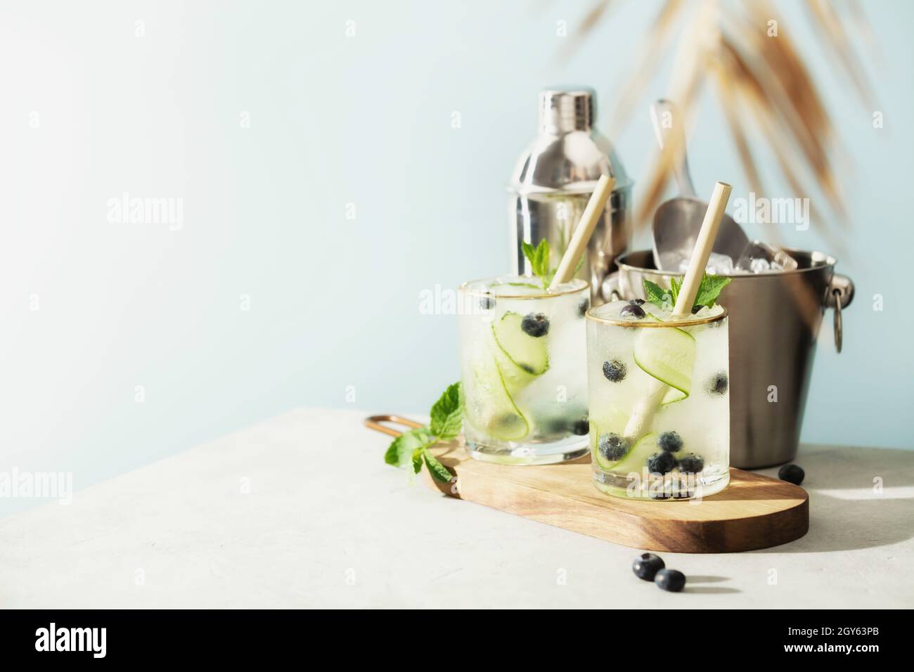Boissons d'été tendance avec concombre, menthe et myrtille et accessoires de bar sur fond bleu ciel Banque D'Images