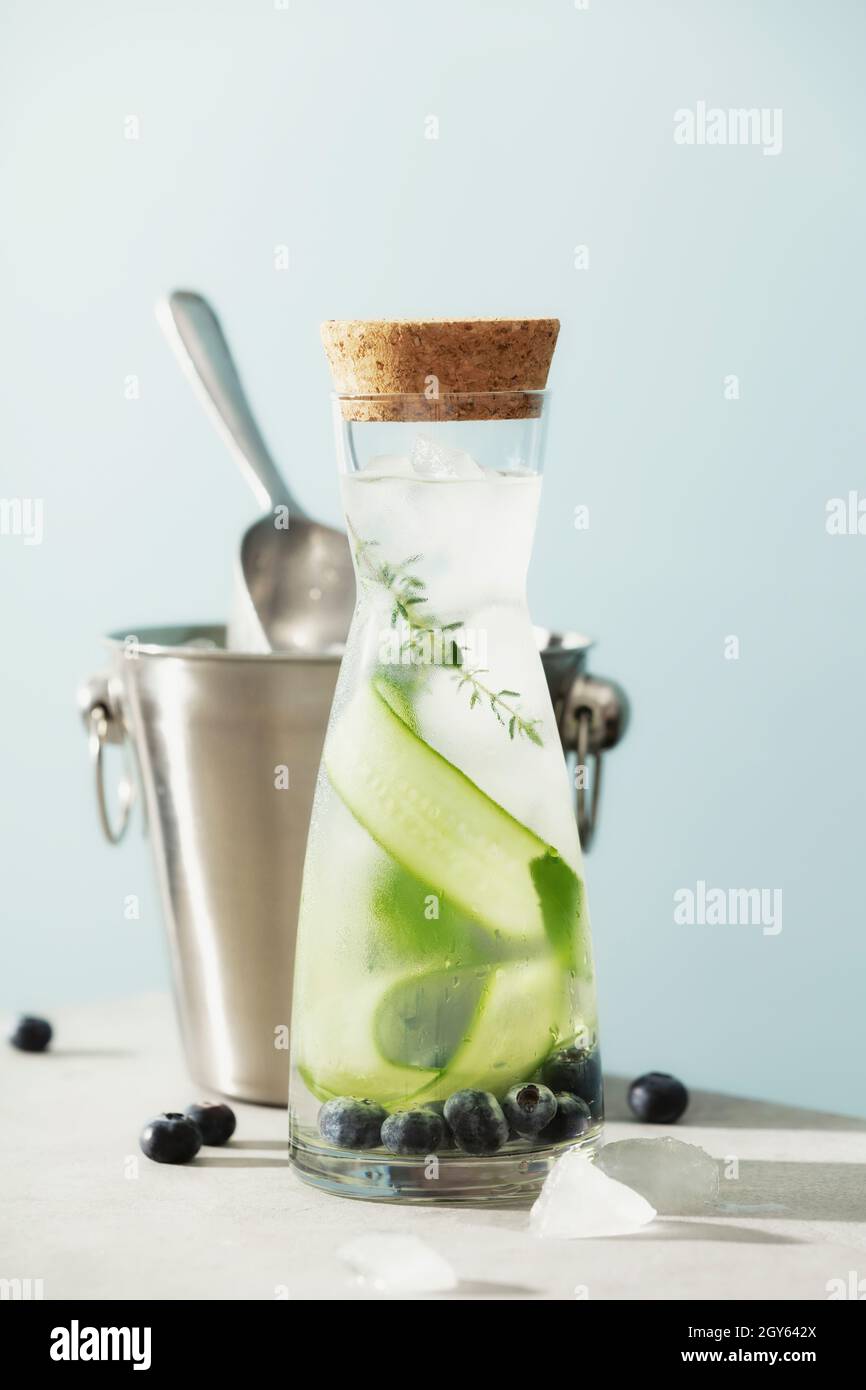 Eau d'été infusée avec concombre, mûre et romarin et seau à glace sur fond bleu ciel Banque D'Images