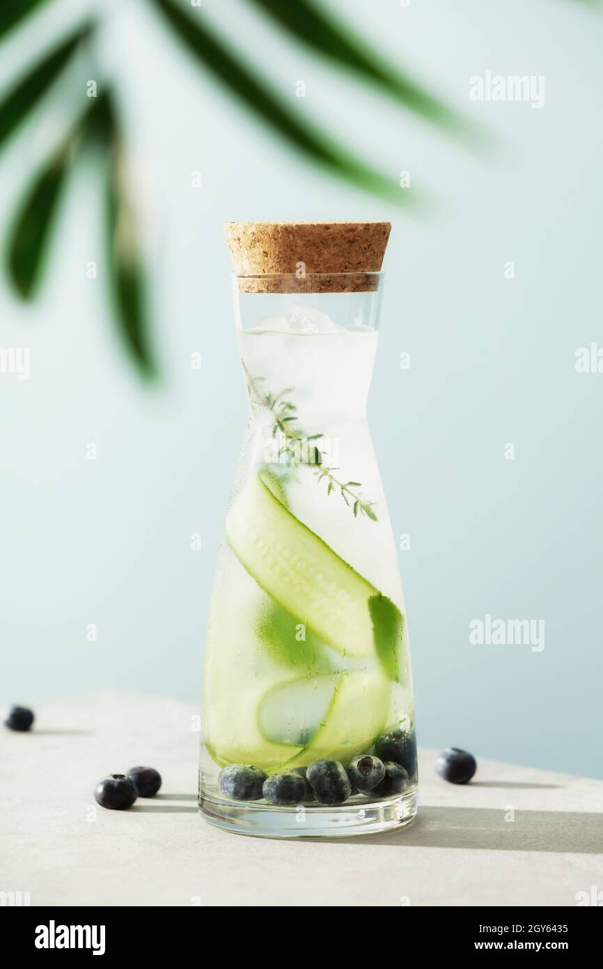 L'eau d'été infusée dans une bouteille tendance avec concombre, mûre et romarin sur fond bleu ciel Banque D'Images