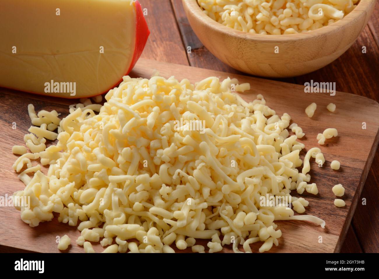 Tas de fromage râpé sur petit panneau en bois. Fromage râpé pour la cuisson sur une planche à découper sur fond de bois Banque D'Images