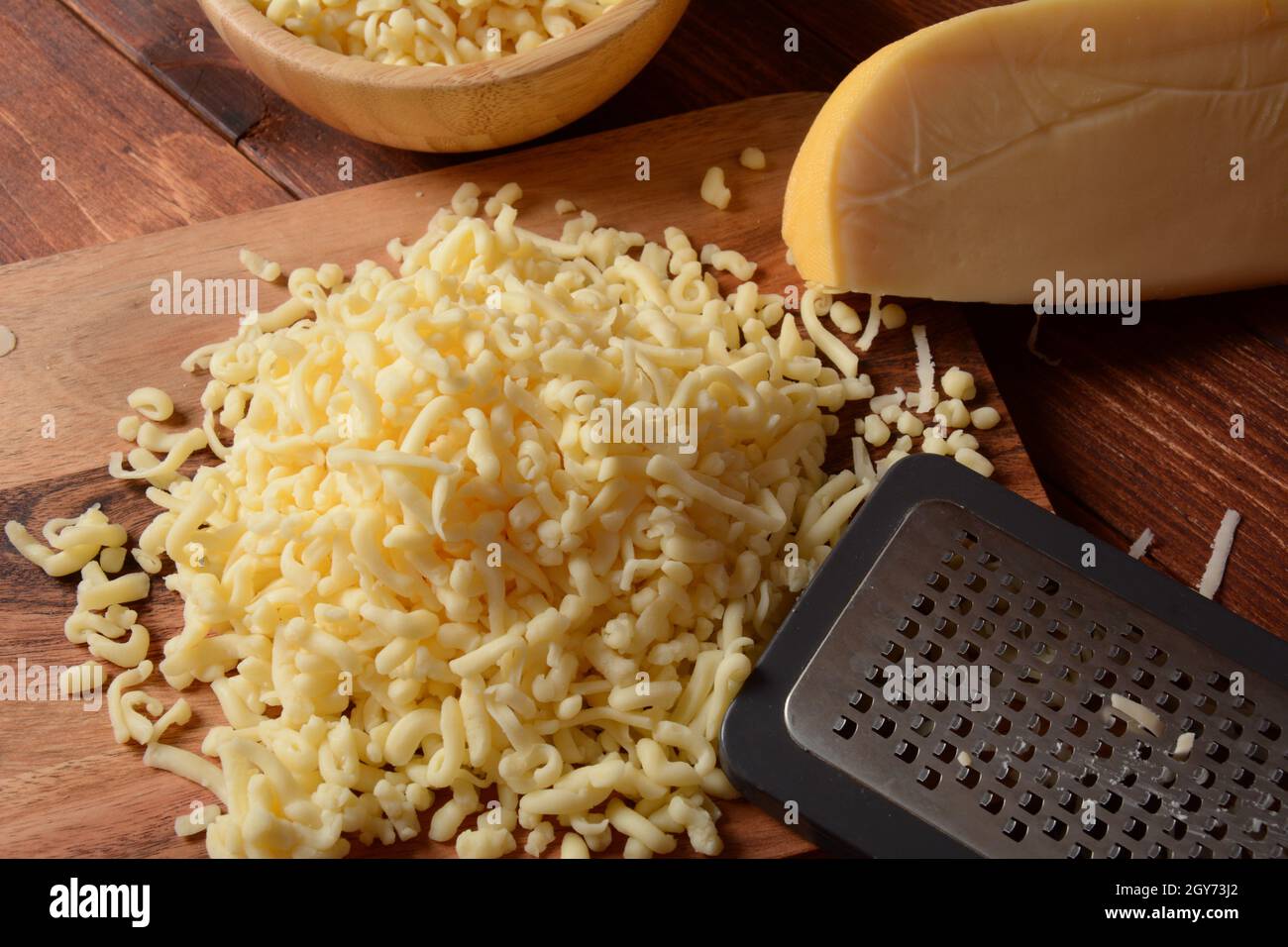 Tas de fromage râpé sur petit panneau en bois. Fromage râpé pour la cuisson sur une planche à découper sur fond de bois Banque D'Images