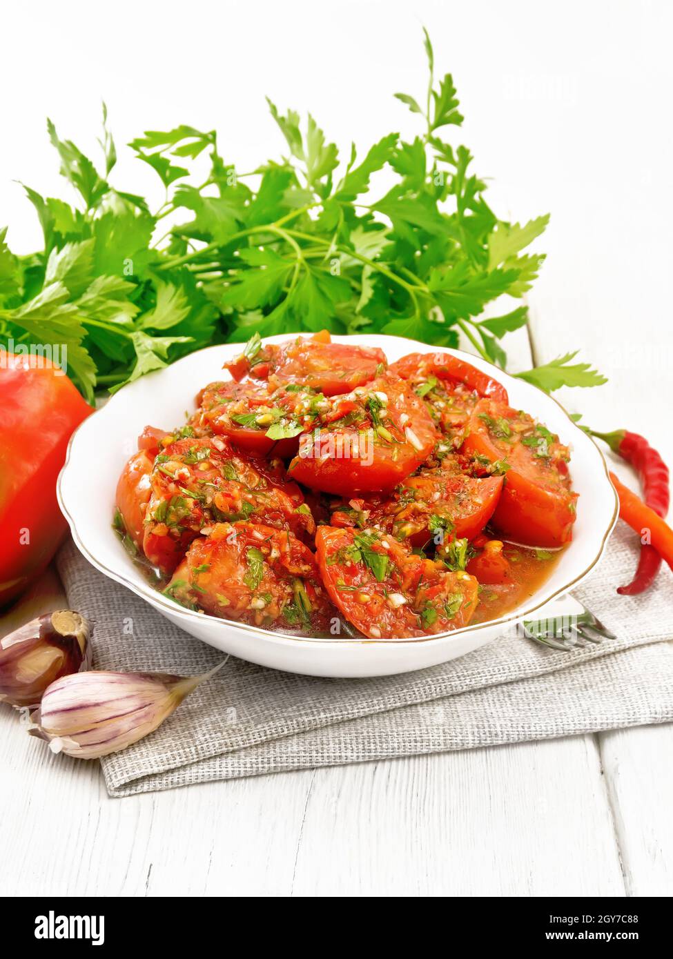 Tomates de style coréen aux poivrons doux et chauds, ail et épices dans une assiette sur une serviette en bois blanc Banque D'Images