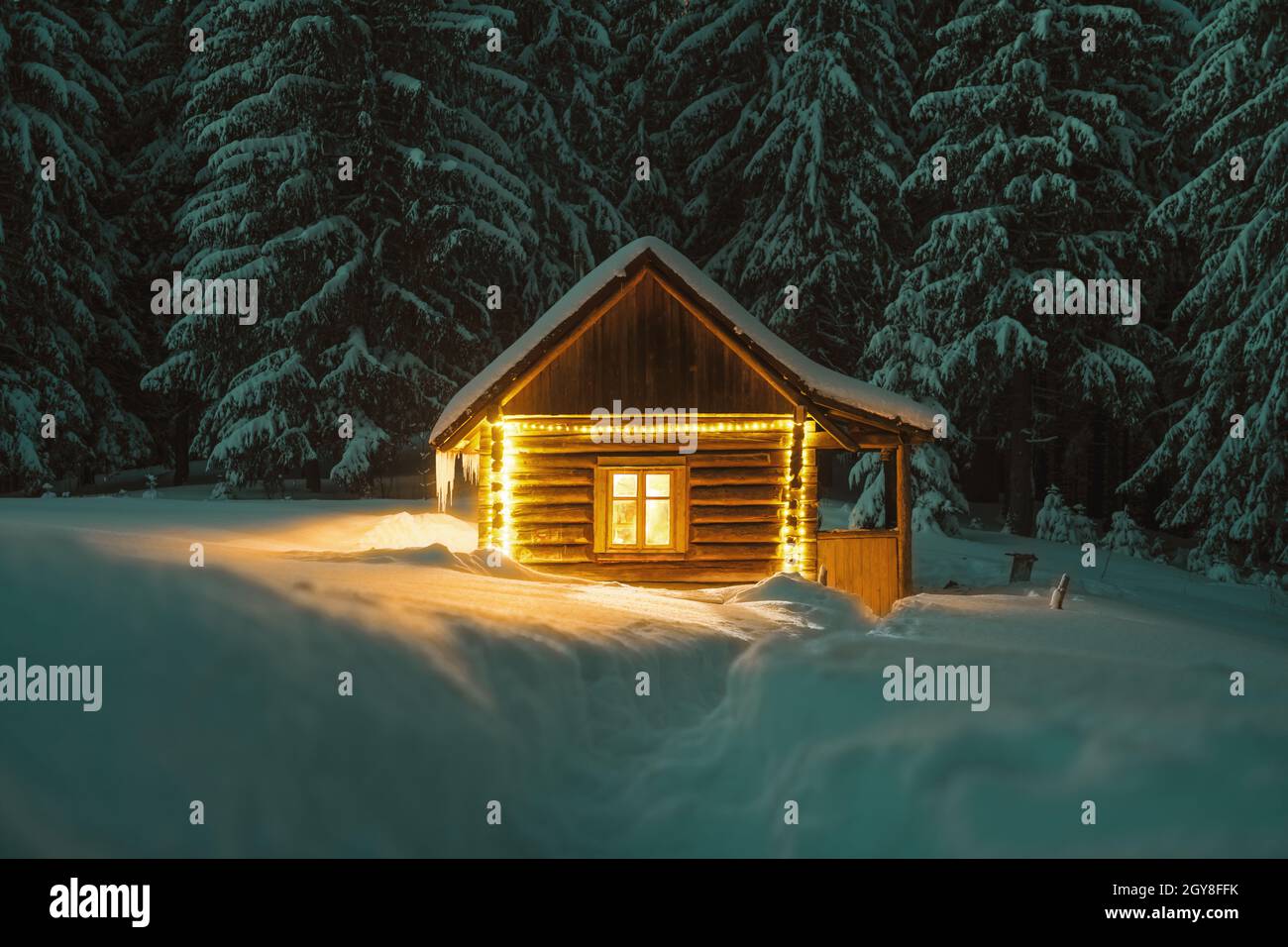 Paysage d'hiver fantastique avec cabine en bois lumineux dans une forêt enneigée. Maison confortable dans les montagnes de Carpathian. Concept de vacances de Noël Banque D'Images