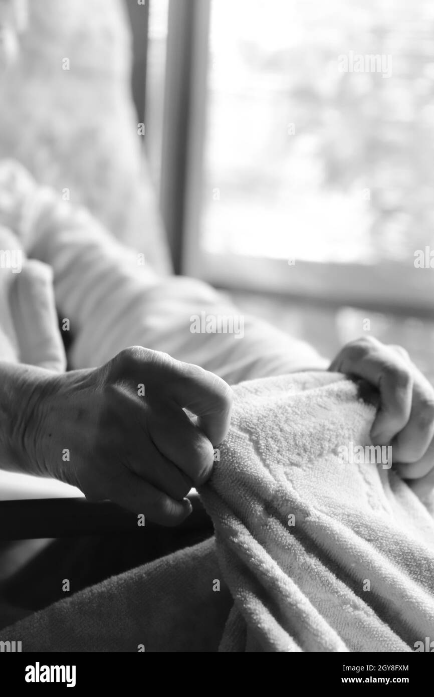 Mains d'une femme âgée atteinte de démence jouant avec une couverture dans un lit de soins infirmiers Banque D'Images