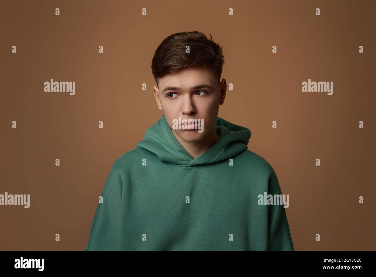 un jeune garçon contrarié dans un sweat-shirt isolé sur fond marron. Émotions humaines, expressions du visage Banque D'Images