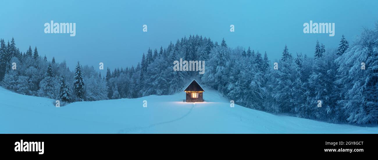 Paysage d'hiver fantastique avec cabine en bois lumineux dans une forêt enneigée.Maison confortable dans les montagnes de Carpathian.Grand panorama.Concept de vacances de Noël Banque D'Images
