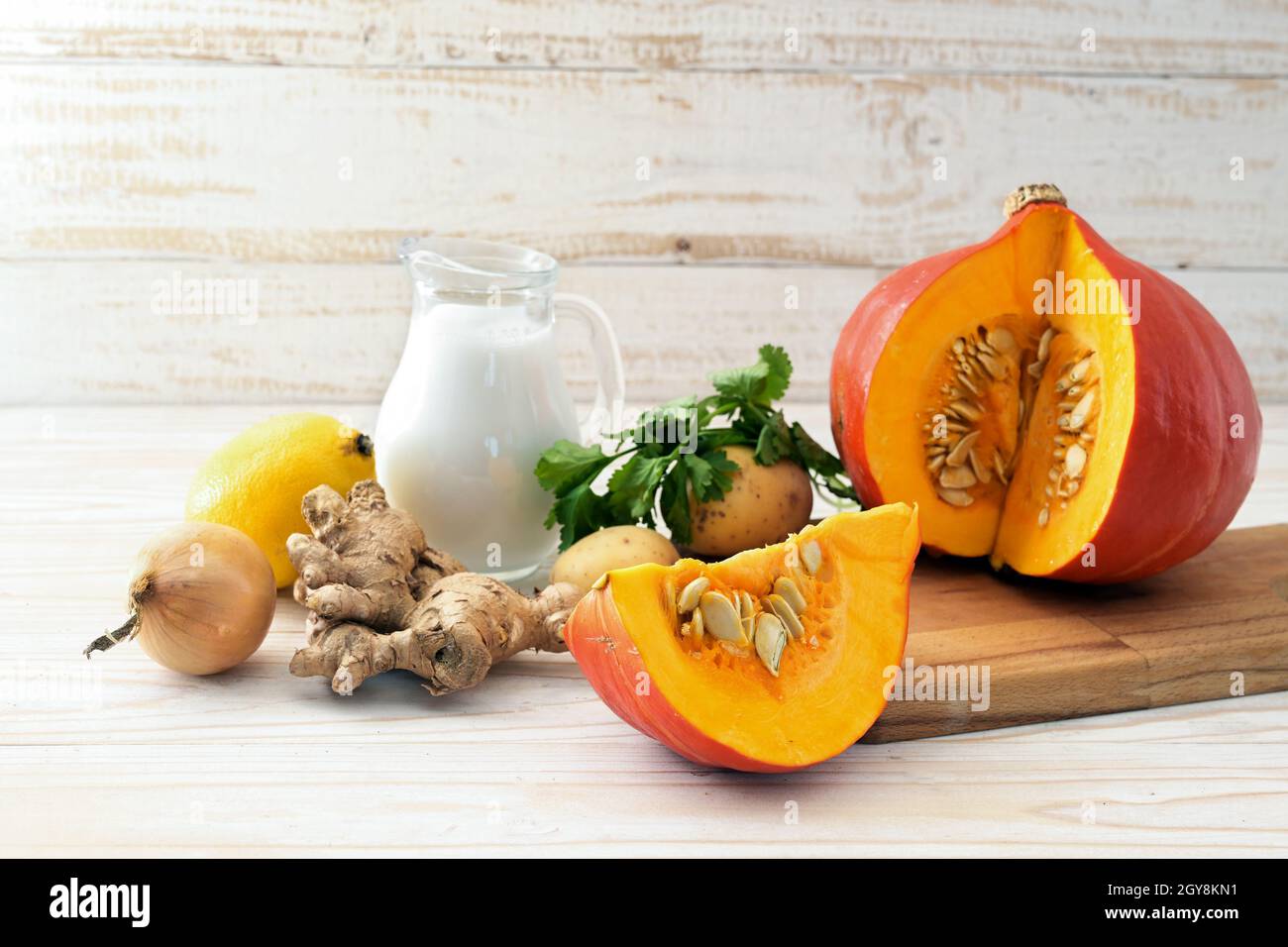 Ingrédients pour une recette de soupe chaude d'automne avec courge rouge kuri, lait de noix de coco et gingembre pour Thanksgiving et Halloween, fond en bois peint blanc Banque D'Images