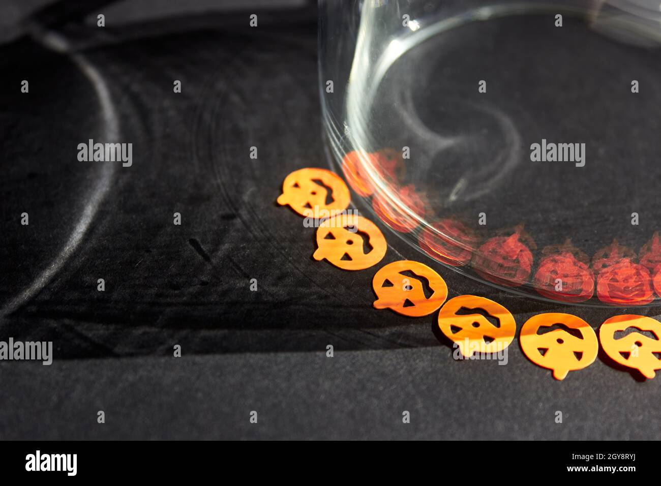 Les petits autocollants orange vif sont reflétés par des ombres effrayantes dans un verre.Citrouilles d'Halloween orange vif sur fond gris foncé. Banque D'Images