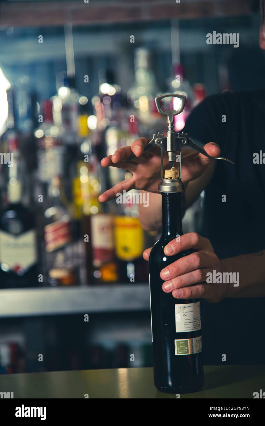 un serveur ouvre une bouteille de vin à l'aide d'un ouvre-vin, sur le comptoir du bar, en bas des bouteilles à l'intérieur du bar Banque D'Images