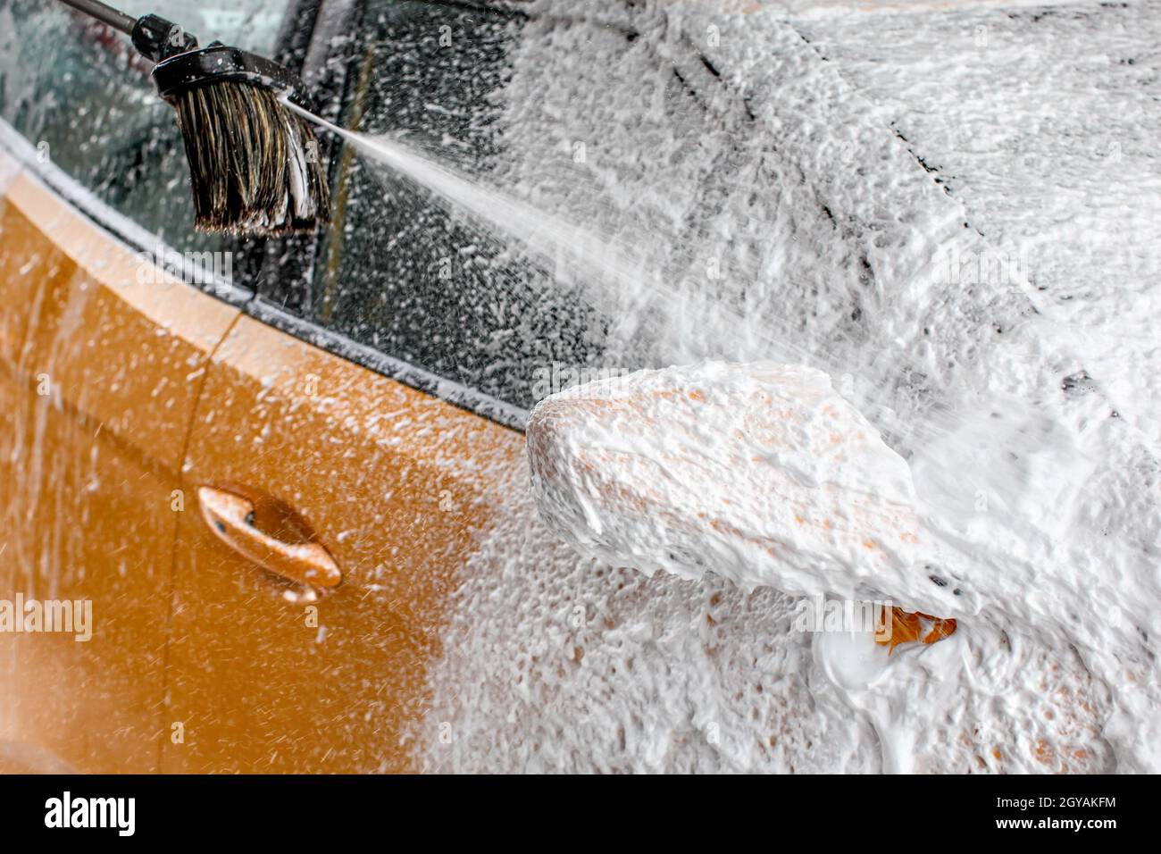 Rétroviseur voiture jaune complètement couverte d'une épaisse couche de mousse de shampooing, plus de pulvérisation le pinceau, lorsque le lavage en lave-auto. Banque D'Images