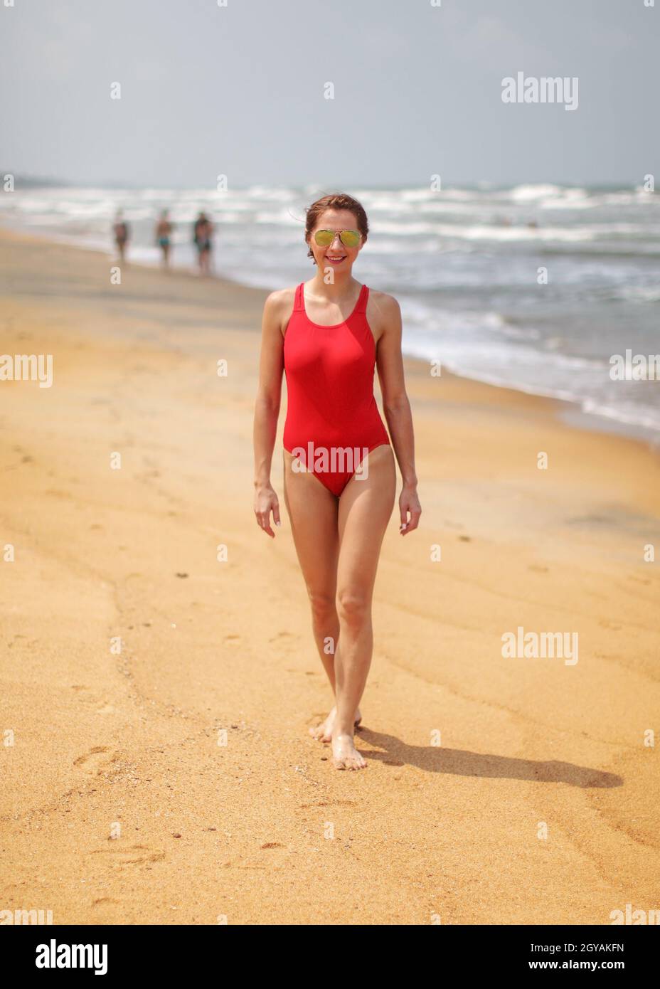 Jeune femme avec corps mince, portant des lunettes et maillot de marcher sur une plage. Banque D'Images