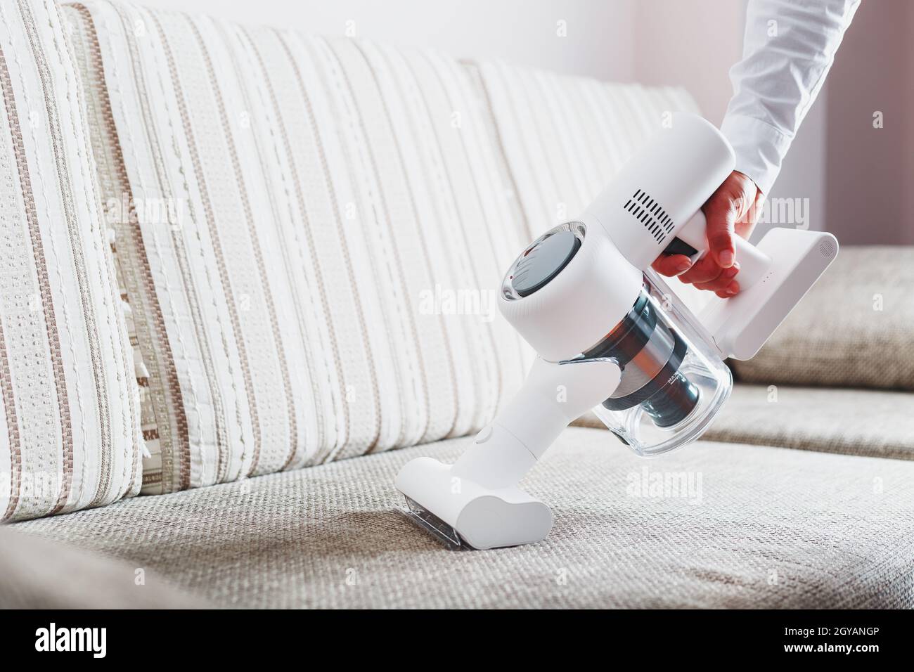 Une personne utilise un aspirateur sans fil blanc pour nettoyer le canapé  du salon Photo Stock - Alamy