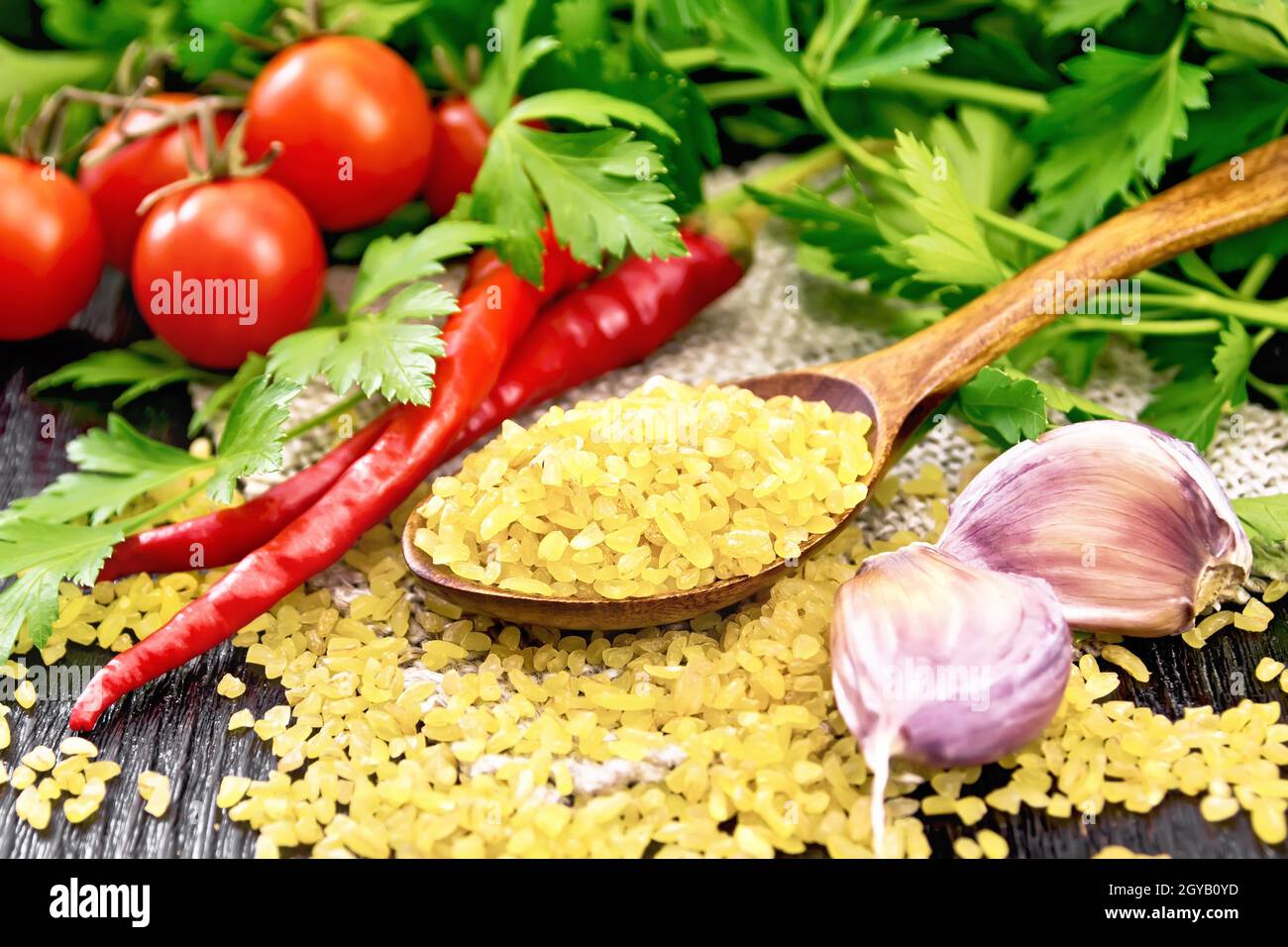 Gruaux bulgur - grains de blé cuits à la vapeur - dans une cuillère sur le germe, les tomates, les poivrons chauds, l'ail et le persil sur fond de bois Banque D'Images