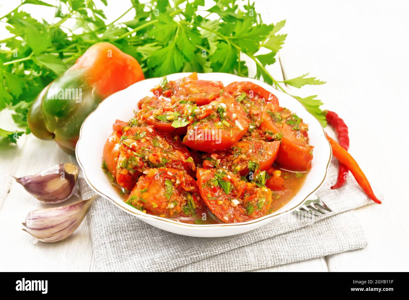 Tomates de style coréen aux poivrons doux et chauds, ail et épices dans une assiette sur une serviette sur le fond de bois léger Banque D'Images