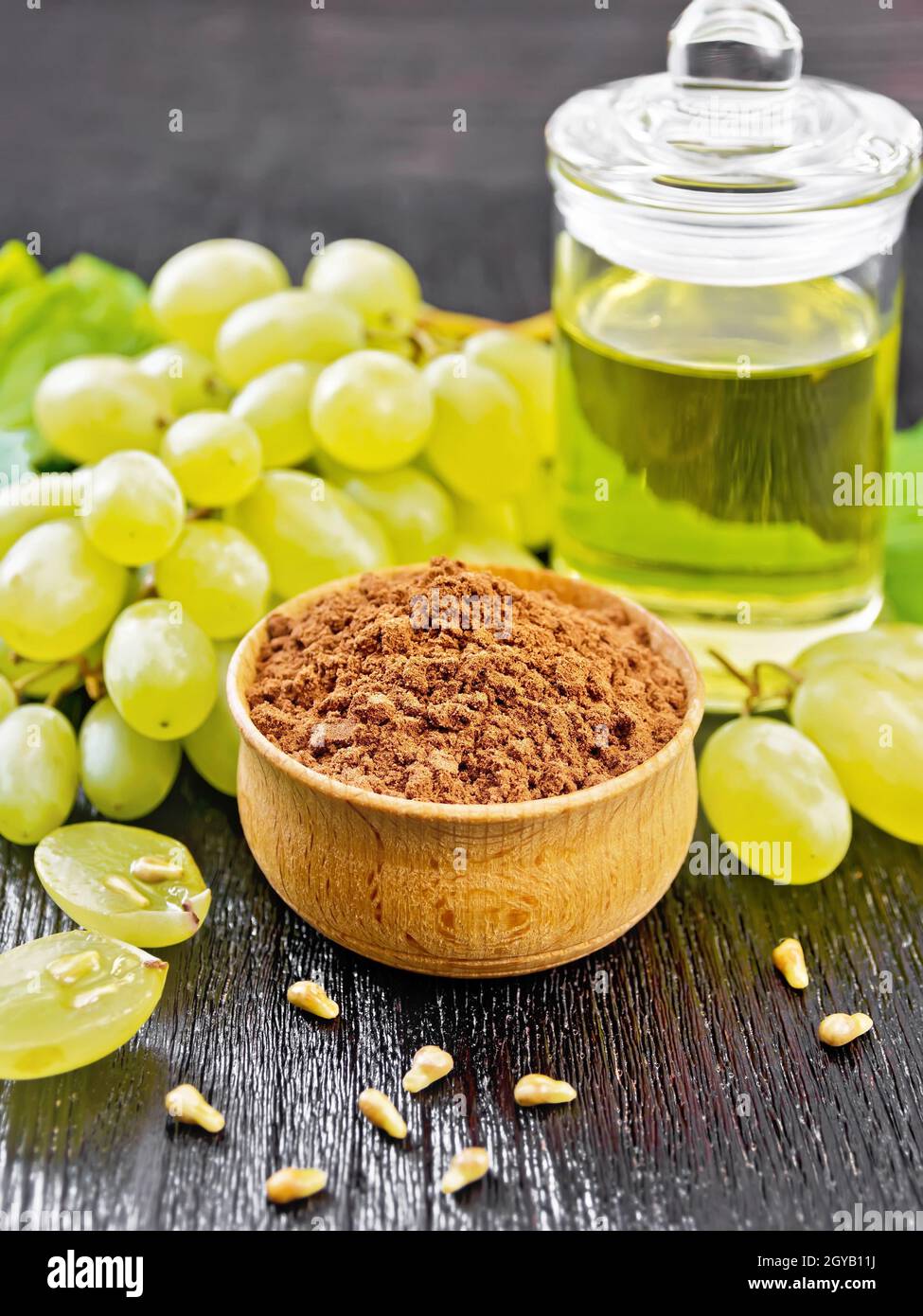 Farine de pépins de raisin dans un bol, huile dans un bocal et baies de raisin sur fond de bois noir Banque D'Images