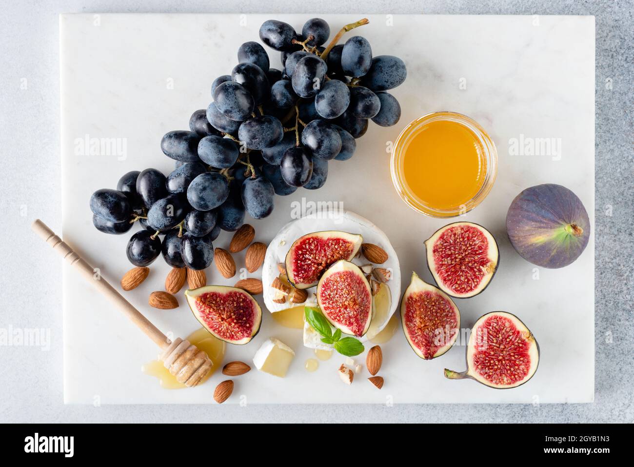 Plateau de fromages Camembert avec figues, raisins, noix et miel.Arrière-plan en marbre, vue du dessus Banque D'Images