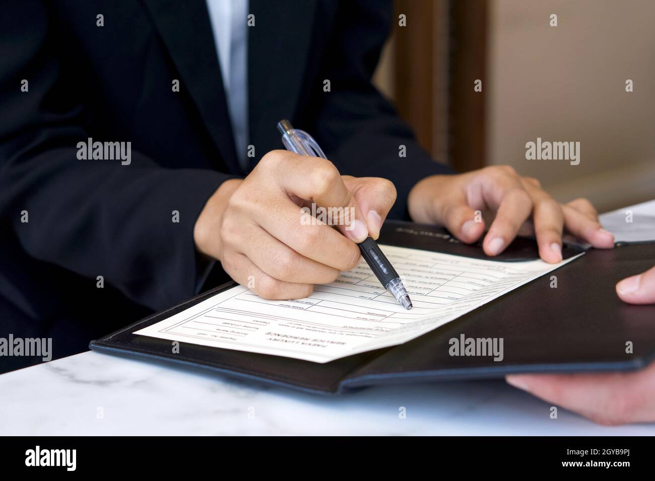 En gros plan, le directeur de l'hôtel tient le stylo, en pointant sur le document d'inscription du client. Banque D'Images