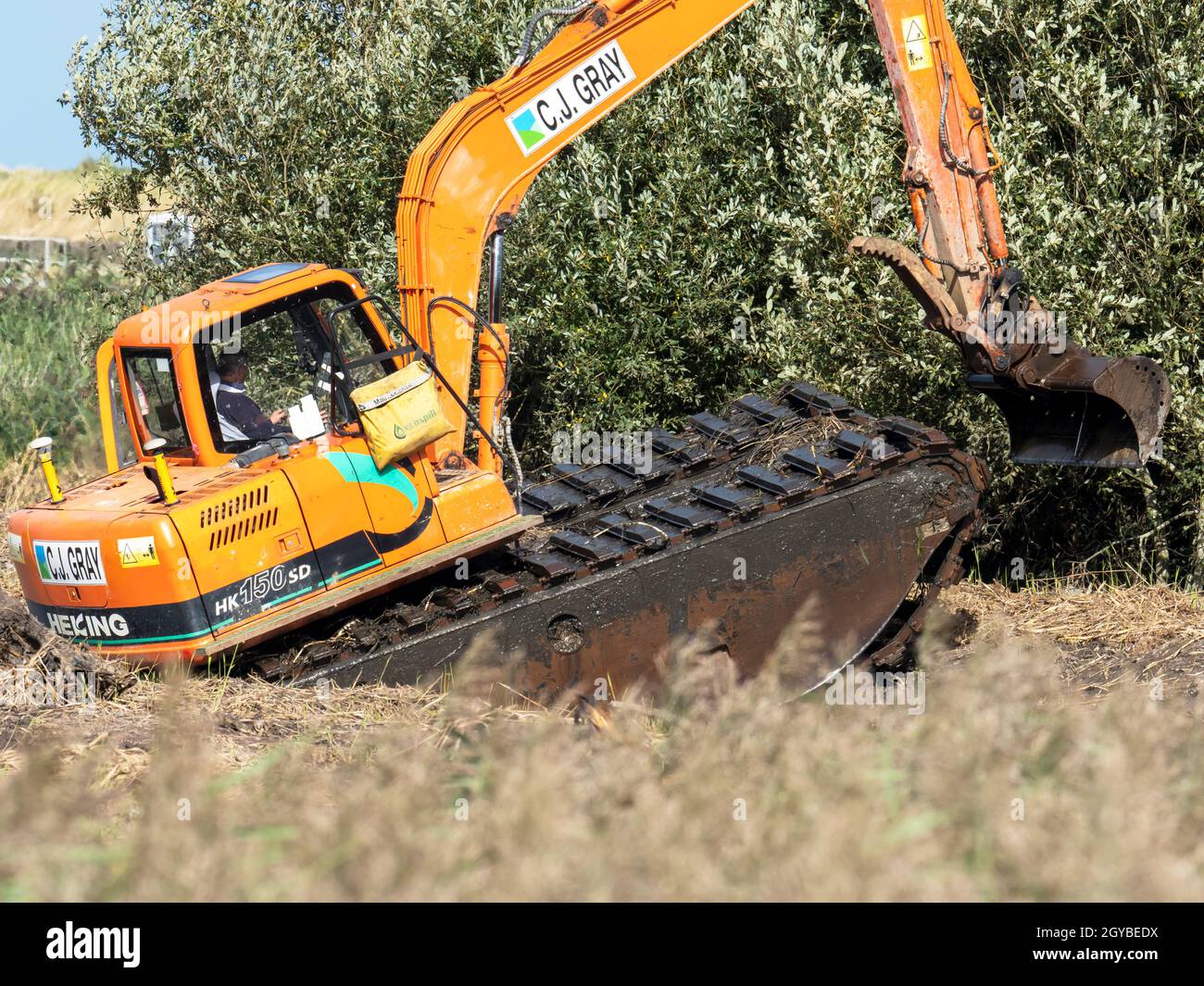 Un creuseur anphibie servant à des travaux de conservation pour créer un nouvel habitat faunique à la réserve de Titchwell RSPB, Norfolk, Royaume-Uni. Banque D'Images