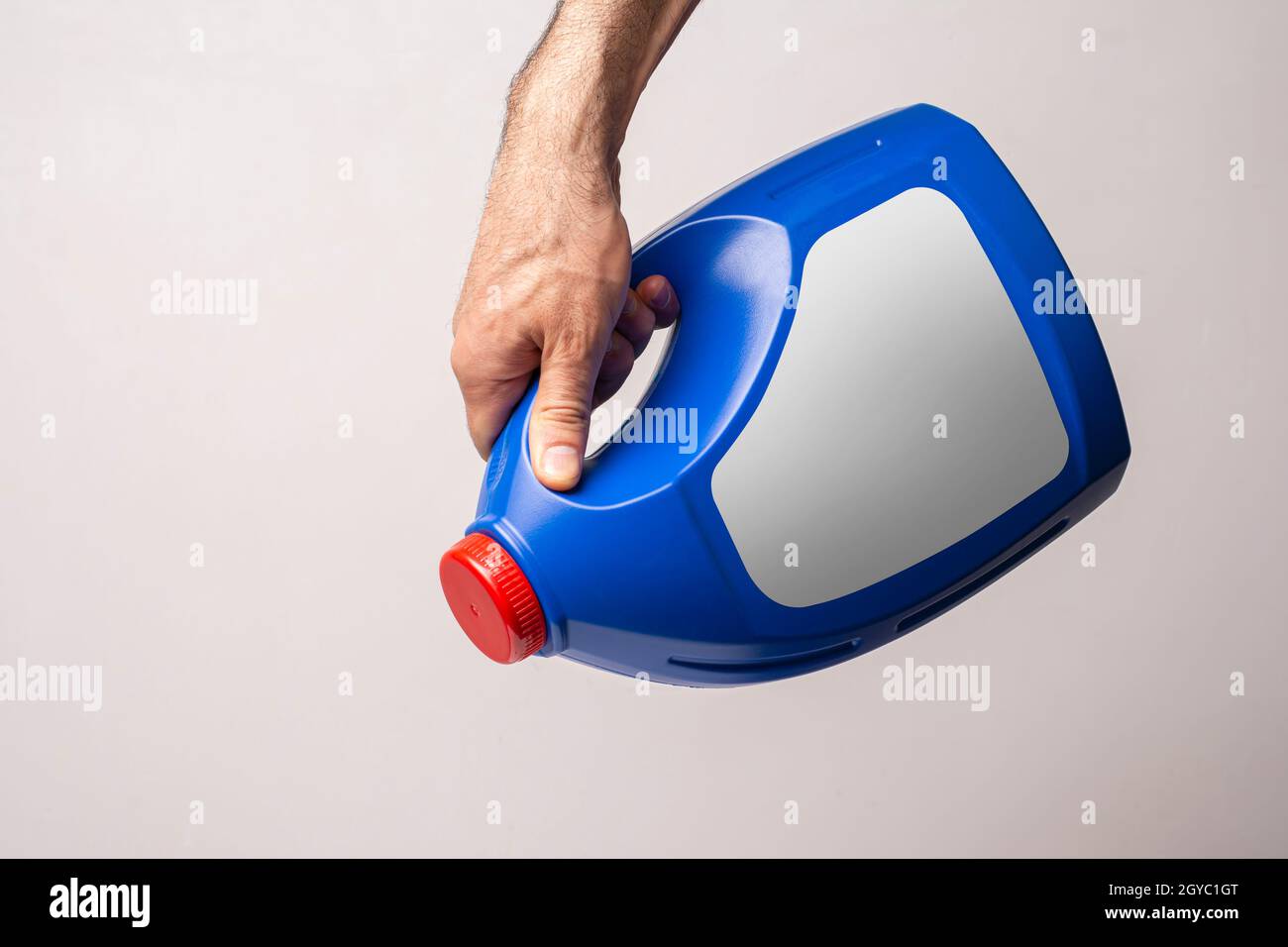 Une main mâle enfermant une bouteille de détergent de cuisine bleue avec bouchon fermé, chemin de sélection de lable inclus. Banque D'Images