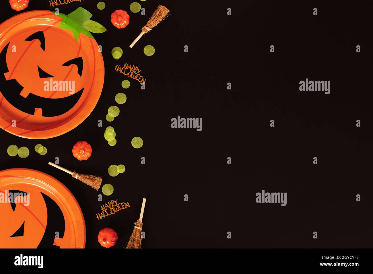 Halloween fête citrouille assiettes en papier, sorcières balais, confetti et heureux Halloween texte côté de fond noir avec espace de copie Banque D'Images