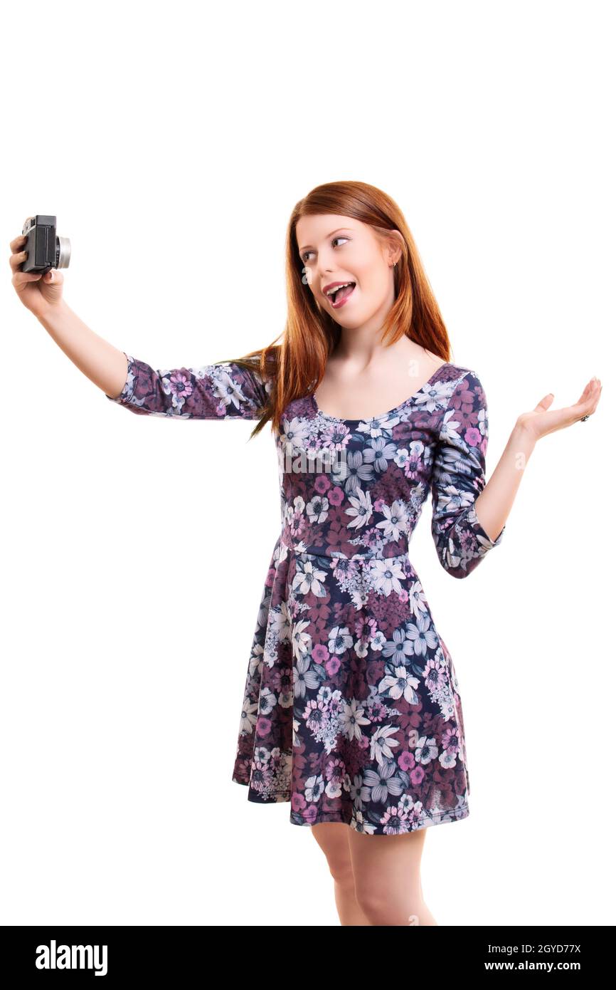 Belle jeune femme dans une robe fleurie prenant un selfie ou filmant son soi-même, isolée sur fond blanc. Belle fille à tête rouge avec cheveux longs vlo Banque D'Images