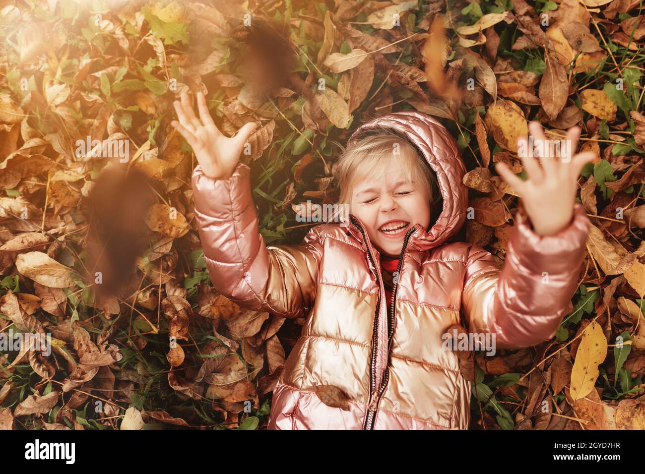 Bonne petite fille blonde joue avec des feuilles d'automne jaunes dans le jardin.L'enfant sourit et s'amuse au parc.Un gamin qui jette des feuilles en automne Banque D'Images