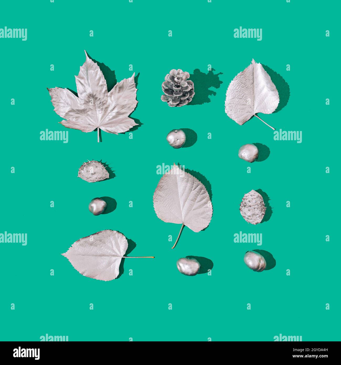 Une infographie faite de feuilles d'argent, de châtaignes et d'un cône de pin sur fond vert.Tendance futuriste des fêtes. Banque D'Images