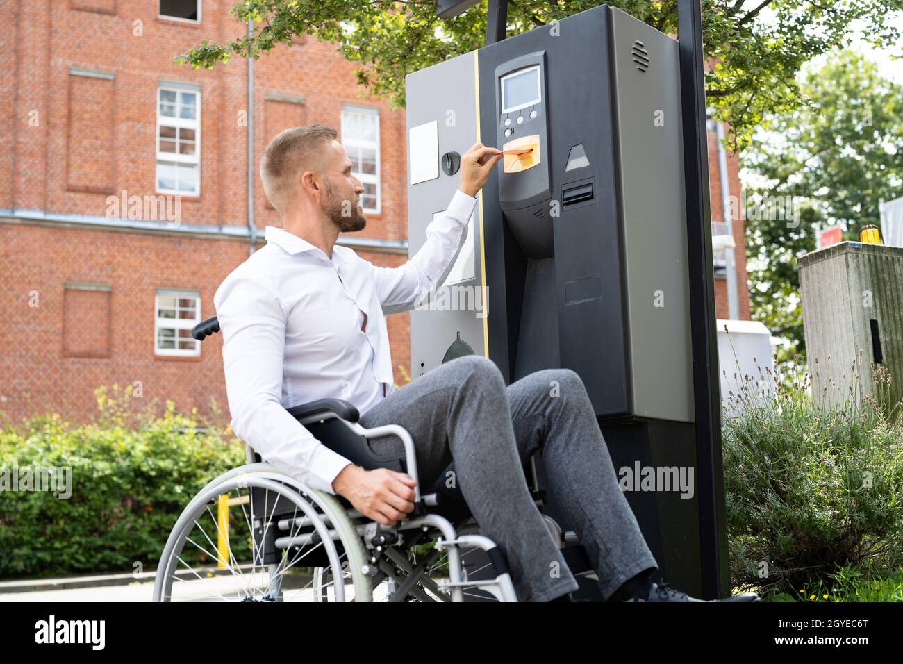 Homme handicapé en fauteuil roulant payant un ticket de parking utilisant la machine Banque D'Images