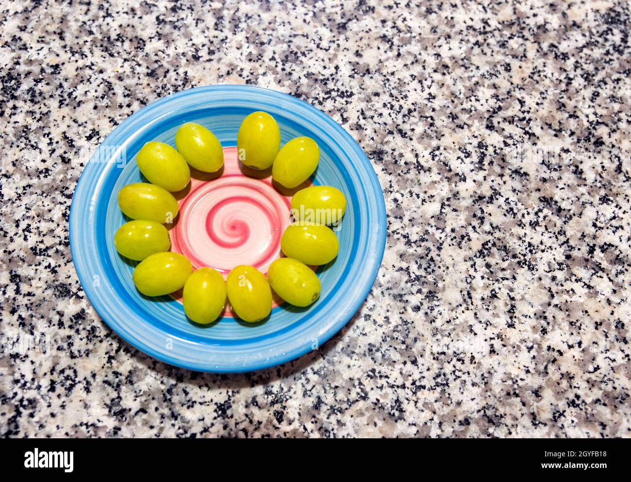 Une assiette bleue décorée d'une spirale rose sur une table en marbre, avec les douze raisins chanceux préparés pour célébrer le nouvel an à la Saint-Sylvestre Banque D'Images
