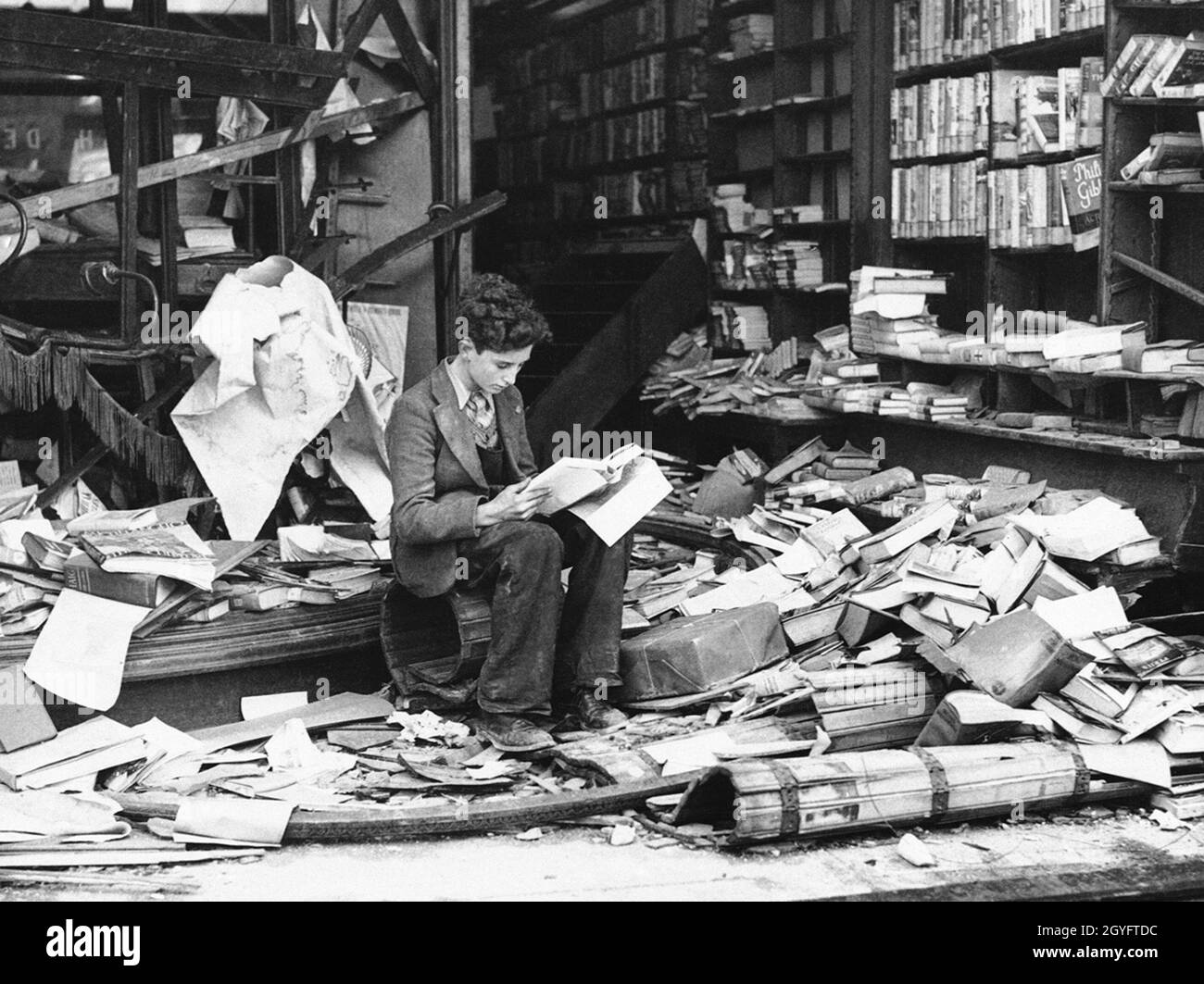 Un jeune garçon s'assit à lire devant les ruines d'une librairie londonienne après un raid aérien pendant le Blitz, Londres 1940 Banque D'Images