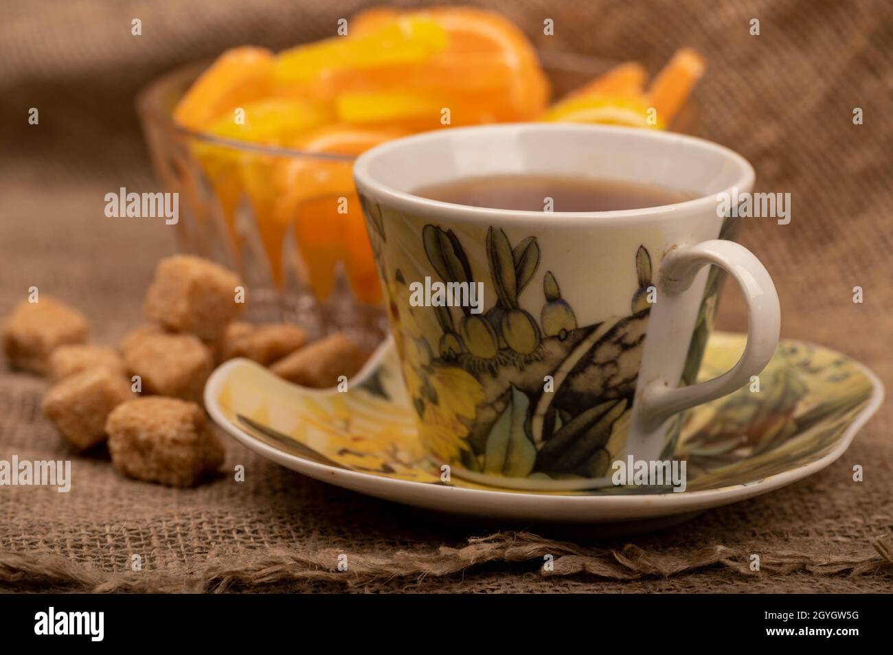 Tranches de citron marmelade multicolores dans un vase en verre, morceaux de sucre de canne brun et une tasse de thé sur une soucoupe, gros plan, sélectif Banque D'Images