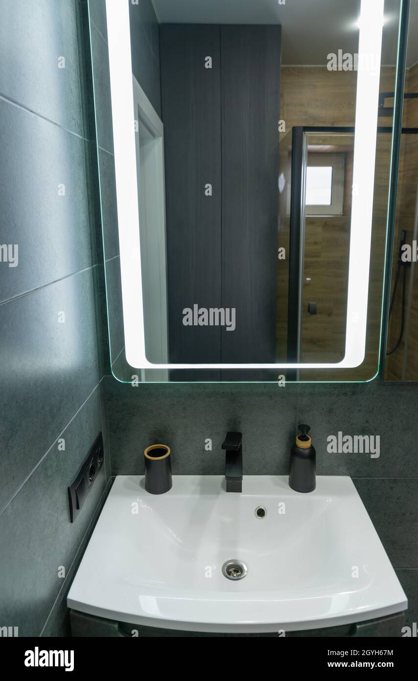 Lavabo blanc simple, meuble-lavabo et miroir dans une salle de bains moderne avec carrelage mural gris avec vue sur une cabine de douche redécorée dans le verre Banque D'Images