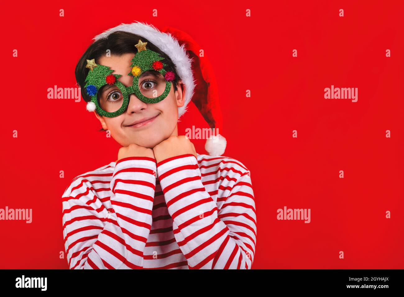 Joyeux Noël.enfant souriant portant chapeau de Père Noël et drôles lunettes de noël sur fond rouge Banque D'Images