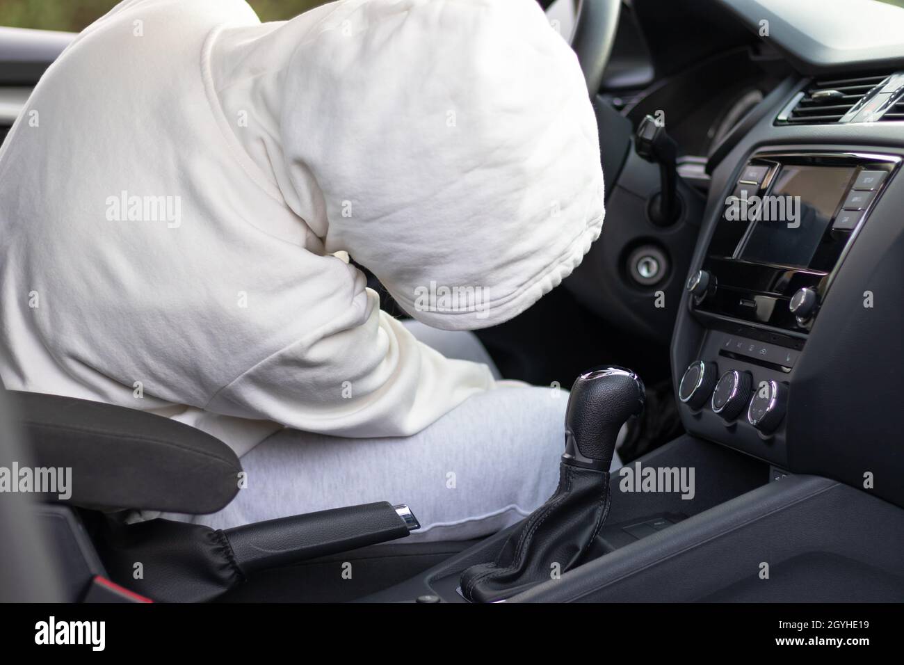 Un homme dans un chandail blanc avec une capuche s'assoit au volant d'une voiture et essaie de la démarrer afin de la voler.Mise au point sélective.Gros plan Banque D'Images