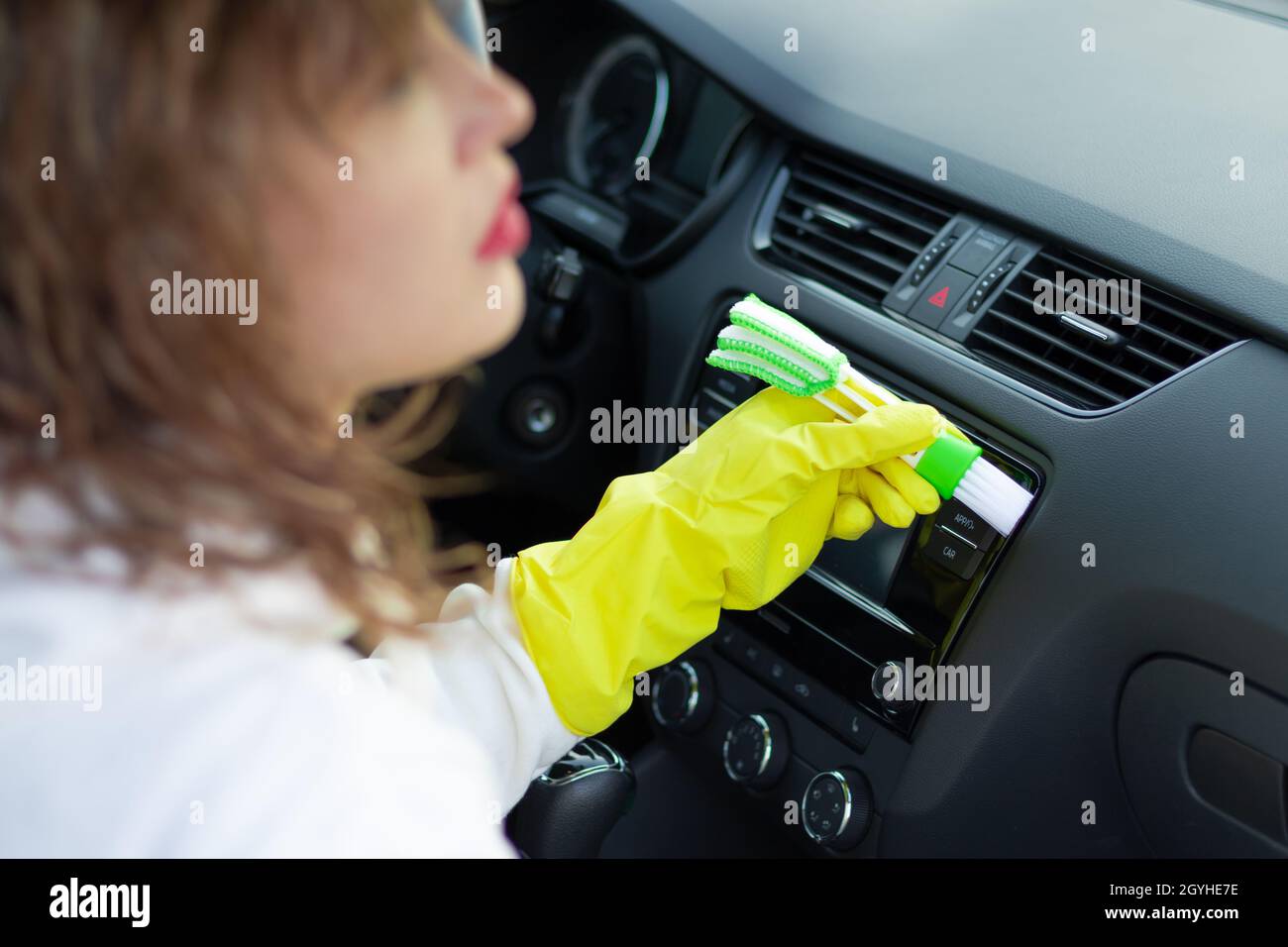Une fille en gants de caoutchouc jaune essuie le tableau de bord d'une voiture de la poussière avec une brosse spéciale lors d'un jour d'automne brillant.Mise au point sélective.Gros plan Banque D'Images