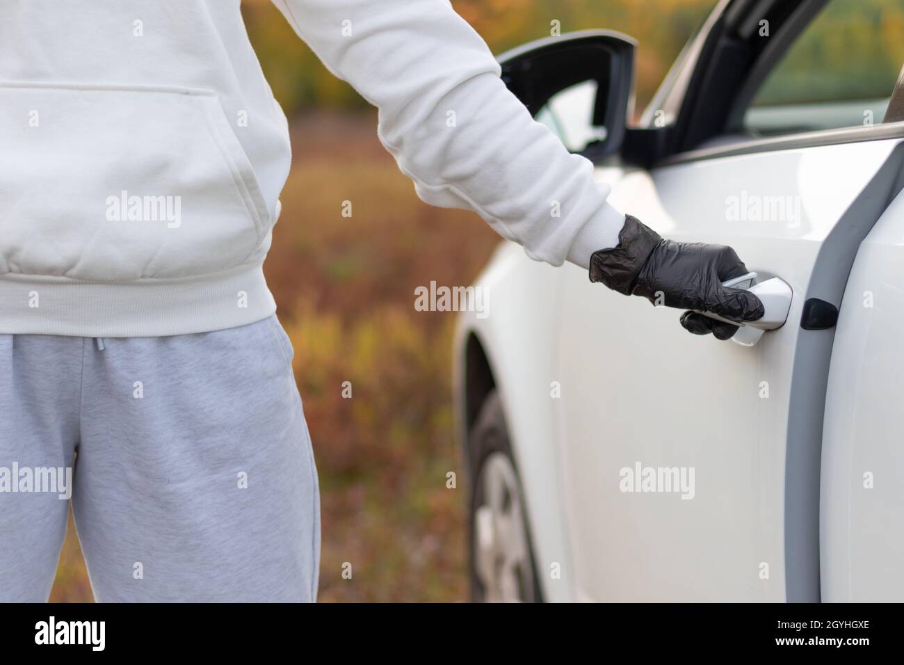 Un homme dans un chandail blanc et des gants noirs ouvre la porte de la voiture pour le voler lors d'une chaude journée d'automne.Mise au point sélective.Gros plan Banque D'Images