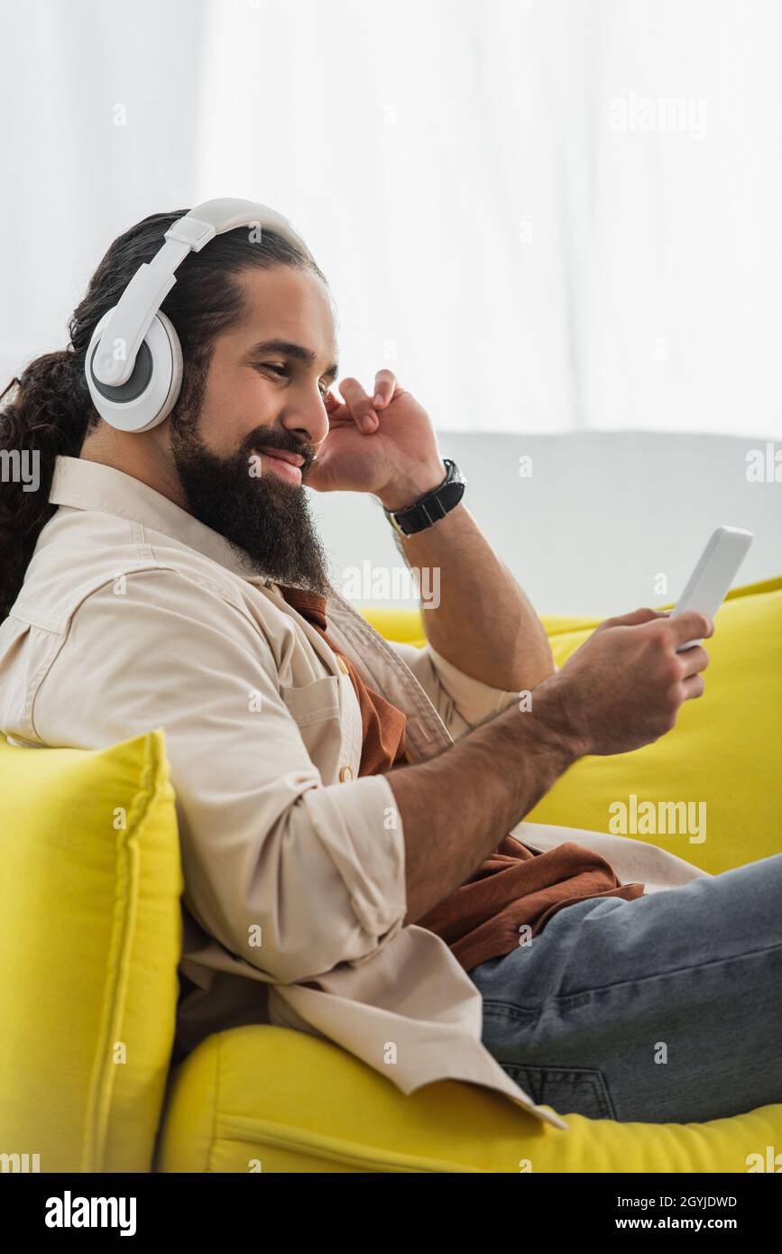 un homme hispanique heureux avec un smartphone qui écoute de la musique dans un casque à la maison Banque D'Images