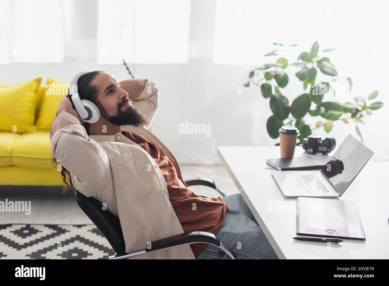 freelance hispanique écoutant de la musique dans des écouteurs tout en se reposant sur le lieu de travail dans un studio à domicile Banque D'Images