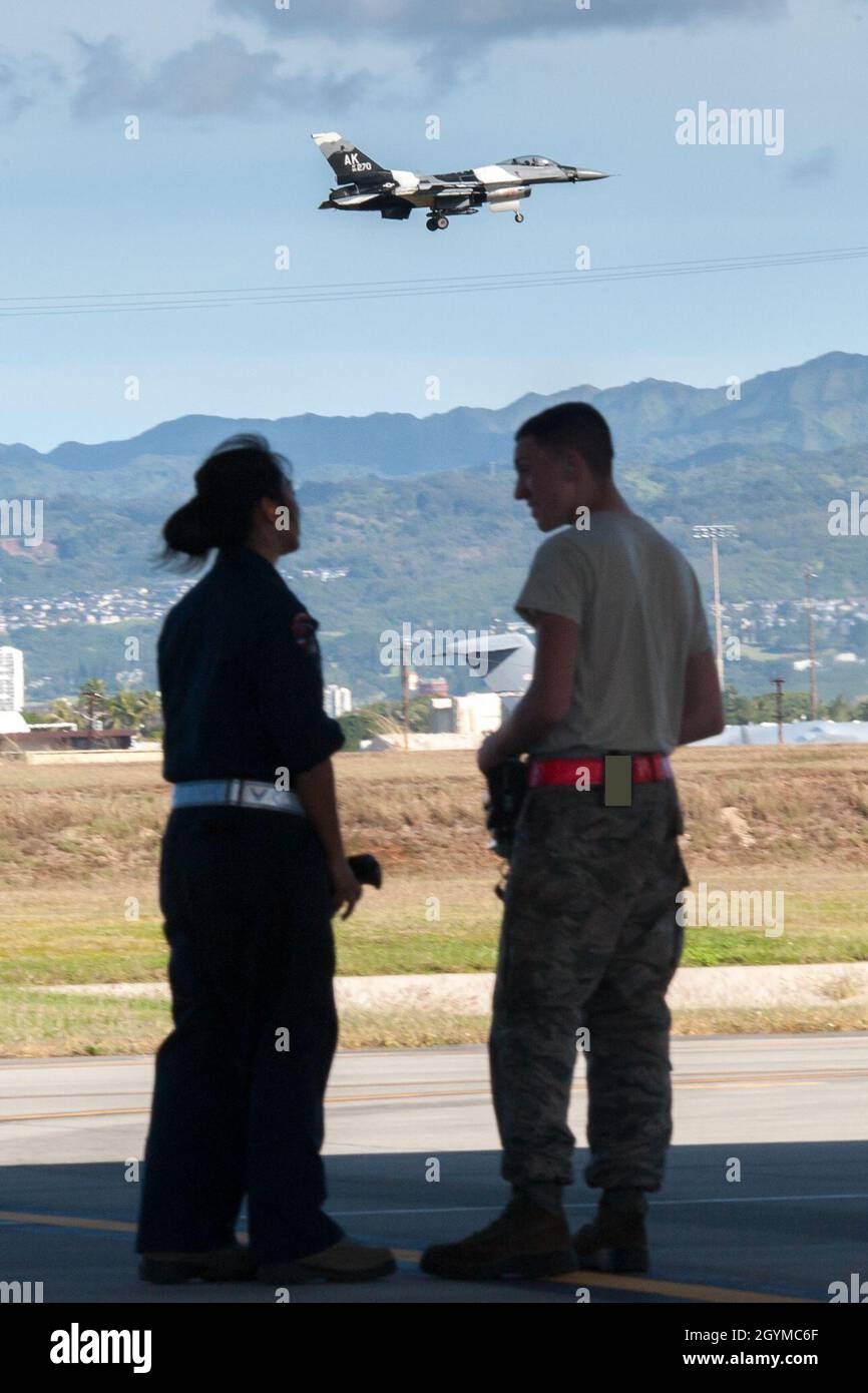 La Garde nationale aérienne d'Hawaï et les chefs d'équipage F-22 Raptor en service actif parlent alors qu'un faucon de combat F-16 approche pour un atterrissage le 30 janvier 2020, à la base conjointe Pearl Harbor-Hickam, Hawaï.Le F-16 est affecté au 18e Escadron d'agresseurs de la base aérienne d'Eielson, en Alaska,Et sa mission est de préparer les pilotes à la victoire en simulant des tactiques de combat susceptibles d’être rencontrées dans le cas d’une bataille aérienne. Chaque mission d’entraînement de Pacific Raptor est effectuée par une équipe d’aviateurs de la Force aérienne active,Composants de la Réserve et de la Garde nationale aérienne.Une partie de cette image était Banque D'Images