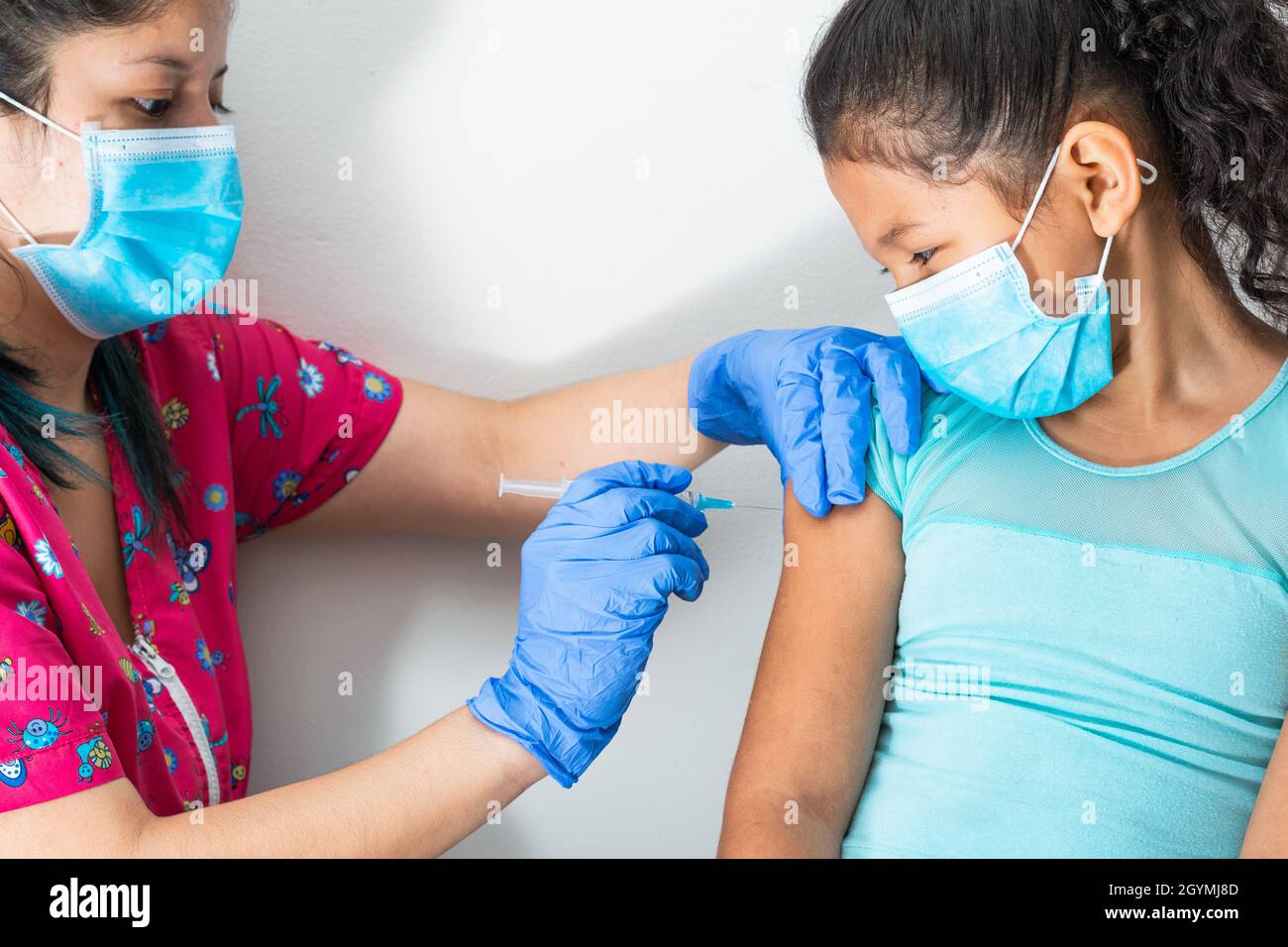 l'infirmière des enfants s'injectant le bras de la petite fille brune, fille qui a peur de l'injection. les mains du médecin avec des gants en caoutchouc injectant le vaccin covid-19 ou le vaccin contre la grippe Banque D'Images