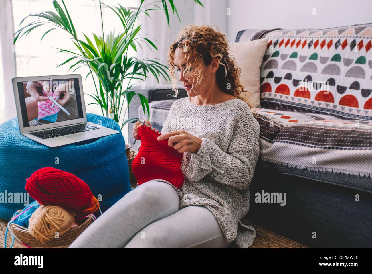 Confortable femme en tricot suivre les conseils en tricot hiver chaud pull  et en pyjama aime le travail en tricot sur une couverture à carreaux rouges  à la maison dans un décor