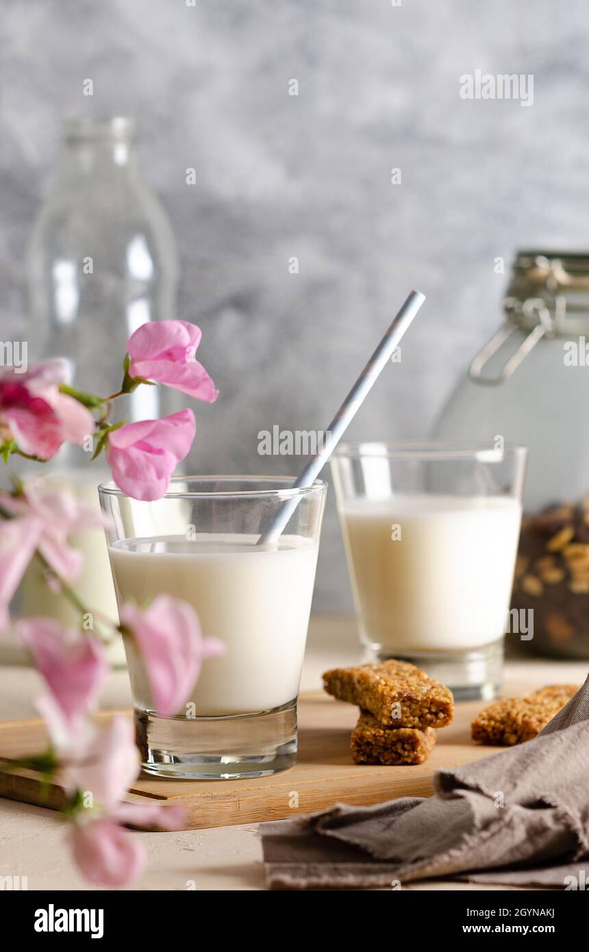 Deux verres et une bouteille de lait, des barres de céréales, quelques noix et raisins secs dans un pot et une serviette brune aux fleurs roses. Banque D'Images