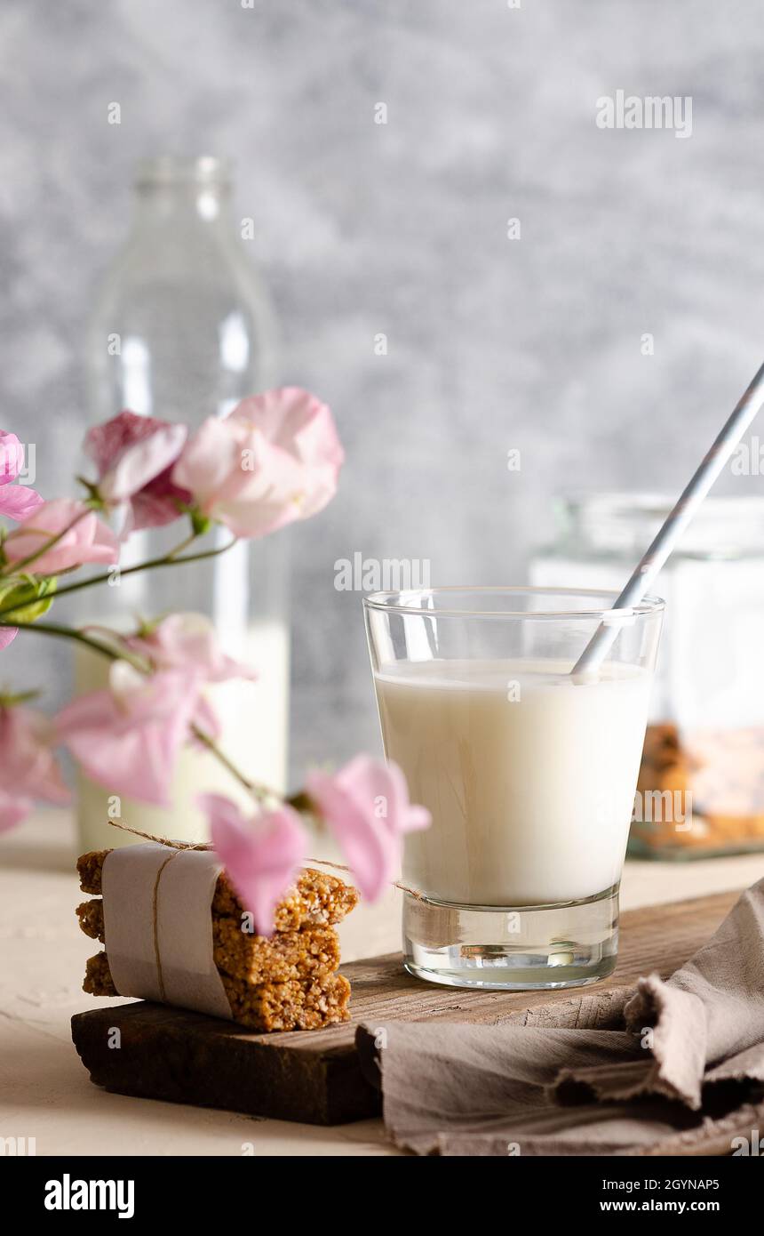 Deux verres et une bouteille de lait, des barres de céréales, quelques noix dans un pot et une serviette brune aux fleurs roses. Banque D'Images