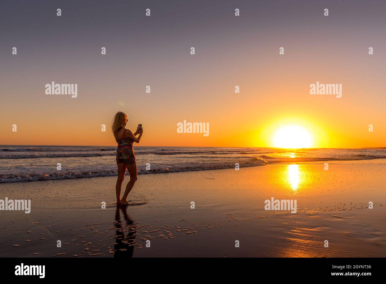 Femme sur la plage photographiant le coucher du soleil. Banque D'Images