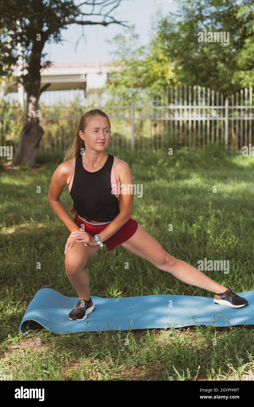 belle femme sportive avec de longs cheveux s'étirant dans le parc avant de courir, assis sur un tapis de sport Banque D'Images